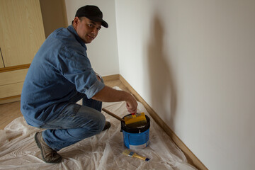 Photo of a handyman wet his paintbrush while whitewashing the walls of his house