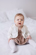 © Tatyana - Sweet  little 1-year-old daughter sitting in bed in beige dress.Portrait of Girl baby child at home. Tenderness and love, sweetness. Lovely family indoors.Serious baby portrait indoors
