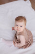 © Tatyana - Sweet  little 1-year-old daughter sitting on chair in grey dress.Portrait of Girl baby child on bed at home. Tenderness and love, sweetness. Lovely family indoors.Serious baby portrait indoors