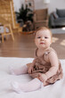 © Tatyana - Sweet  little 1-year-old daughter sitting on chair in grey dress.Portrait of Girl baby child on bed at home. Tenderness and love, sweetness. Lovely family indoors.Serious baby portrait indoors
