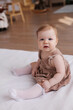 © Tatyana - Sweet  little 1-year-old daughter sitting on chair in grey dress.Portrait of Girl baby child on bed at home. Tenderness and love, sweetness. Lovely family indoors.Serious baby portrait indoors