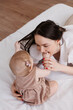 © Tatyana - Sweet young mother playing with her little 1-year-old daughter in bed.Caring brunette woman laying with her baby child at home. Tenderness and love between mother and daughter. Lovely family indoors.