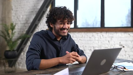 Wall Mural - Video call concept, virtual meeting. Young middle eastern guy relaxed sitting at the table and talking online via video call with group of friends or employees. Man waving to the camera