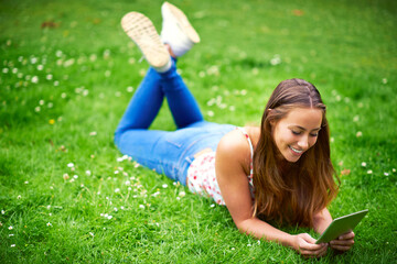 Canvas Print - Stumbling upon some great websites. Shot of a young woman using her digital tablet while lying on the grass at the park.