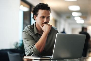 Wall Mural - I know I can make this better. Shot of a handsome young businessman sitting alone in the office and looking contemplative while using his laptop.