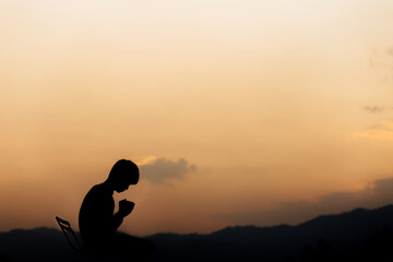 Silhouette of a man holding hands and prayer on mountain at sunset. concept of religion.