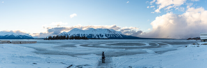 Single person standing on a frozen lake scenery in northern Canada during winter with snow capped mountains background in Atlin, British Columbia