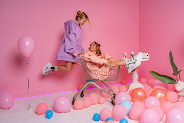 Two beautiful attractive funny joyful cheerful relaxed carefree girls dressed in casual fashion clothes isolated on hot pink background