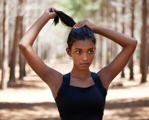 Hair up, lets train. Shot of an attractive young woman standing alone outside and tying her hair before her workout.