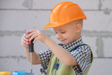 Child play with supplies, tools saw, hammer, screwdriver, helmet, builder, carpenter. Kids playing in the profession. Little repairman. Kid boy in builders uniform and helmet with repair tools.