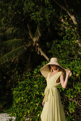 Wall Mural - Beautiful young woman in long green dress and straw hat on Seychelles beach on Mahe or La Digue island