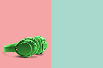 Poster - Computer headphones. Green headphones on a green-red pastel background. The concept of listening to music, creating audio, music. Computer work, abstraction and minimalist style.