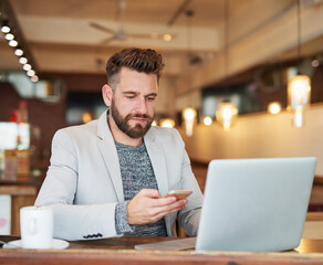 Poster - I should save this number.... Cropped shot of a modern businessman using his laptop and cellphone in a coffee shop.