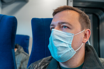 Wall Mural - Portrait of male passenger wearing medical face mask in public transportation. Millennial man looking away at window, thinking, going to home by train during coronavirus pandemic. New normal