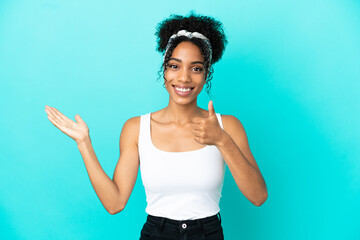 Sticker - Young latin woman isolated on blue background holding copyspace imaginary on the palm to insert an ad and with thumbs up