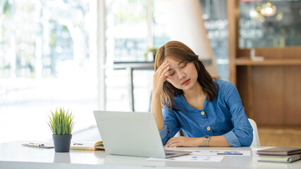 Asian women sitting in an office with stress and eye strain tired, portrait of sad unhappy tired frustrated disappointed lady suffering from migraine sitting at the table, Sick worker concept.