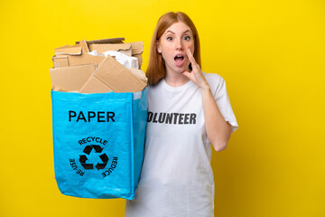 Wall Mural - Young redhead woman holding a recycling bag full of paper to recycle isolated on yellow background with surprise and shocked facial expression