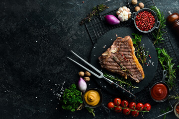 porterhouse steak or T Bone Steak dry aged of beef Ready to Cook on wooden Board with herbs, pepper and salt. On a black stone background.