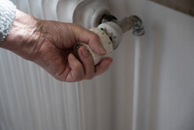 A Senior Woman's Hand Turning The Knob On An Old Radiator To Adjust The Temperature