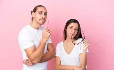 Wall Mural - Young caucasian couple isolated on pink background With glasses with happy expression