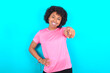 © Roquillo - young girl with afro hairstyle wearing pink T-shirt over blue background pointing at camera with a satisfied, confident, friendly smile, choosing you