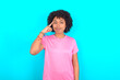 © Roquillo - young girl with afro hairstyle wearing pink T-shirt over blue background tries to memorize something, keeps fore finger on temple, reminds information for exam,