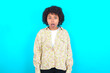 © Roquillo - Oh my God. Surprised young girl with afro hairstyle wearing floral shirt over blue background stares at camera with shocked expression exclaims with unexpectedness,