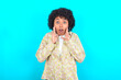 © Roquillo - young girl with afro hairstyle wearing floral shirt over blue background shouting excited to front.