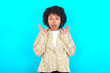 © Roquillo - Surprised terrified young girl with afro hairstyle wearing floral shirt over blue background Gestures with uncertainty, stares at camera, puzzled as doesn't know answer on tricky question,