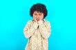 © Roquillo - young girl with afro hairstyle wearing floral shirt over blue background Tired hands covering face, depression and sadness, upset and irritated for problem