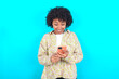 © Roquillo - young girl with afro hairstyle wearing floral shirt over blue background using mobile phone chatting free time .