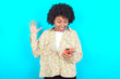 © Roquillo - young girl with afro hairstyle wearing floral shirt over blue background holding in hands cell reading browsing news
