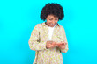 © Roquillo - young girl with afro hairstyle wearing floral shirt over blue background holding in hands cell playing video games or chatting