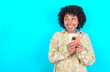 © Roquillo - young girl with afro hairstyle wearing floral shirt over blue background holding in hands showing new cell