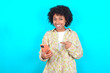 © Roquillo - young girl with afro hairstyle wearing floral shirt over blue background holding in hands showing new cell,