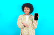 © Roquillo - young girl with afro hairstyle wearing floral shirt over blue background with a mobile. presenting smartphone. Advertisement concept.