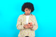 © Roquillo - Focused young girl with afro hairstyle wearing floral shirt over blue background use smartphone reading social media news, or important e-mail