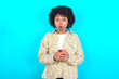 © Roquillo - Shocked young girl with afro hairstyle wearing floral shirt over blue background opens mouth hold phone reading advert unbelievable big shopping prices