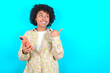 © Roquillo - young girl with afro hairstyle wearing floral shirt over blue background using and texting with smartphone  pointing and showing with thumb up to the side with happy face smiling