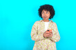 © Roquillo - young girl with afro hairstyle wearing floral shirt over blue background holds telephone hands reads good youth news look empty space advert