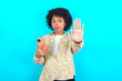 © Roquillo - young girl with afro hairstyle wearing floral shirt over blue background using and texting with smartphone with open hand doing stop sign with serious and confident expression, defense gesture