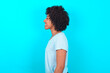 © Roquillo - Profile portrait of nice Young woman with afro hairstyle wearing blue T-shirt over blue background look empty space toothy smile