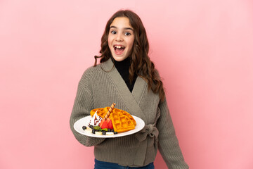 Wall Mural - Little girl holding waffles isolated on pink background with surprise facial expression