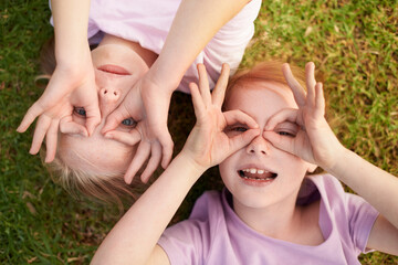 We see you. Two little girls lying on their backs making circles around their eyes with their hands.