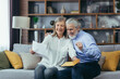 © Liubomir - Happy senior retired couple sitting on sofa at home reading letter, happy and smiling