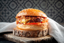 A Plump Burger With Beef, Fried Onions, Cheese, Tomatoes And Barbecue Sauce On A Wooden Board. Cheeseburger With Sesame Bun