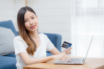 Wall Mural - Young asian woman sit on sofa using laptop computer shopping online with credit card buying to internet, happy girl payment with e-business on couch, purchase and payment, business concept.