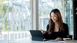 © kamiphotos - A beautiful Asian businesswoman sitting in her private office, she is checking company financial documents, she is a female executive of a startup company. Concept of financial management.
