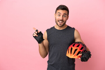 Wall Mural - Young cyclist man isolated on pink background pointing finger to the side