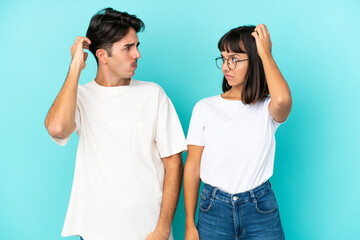 Young mixed race couple isolated on blue background having doubts while scratching head